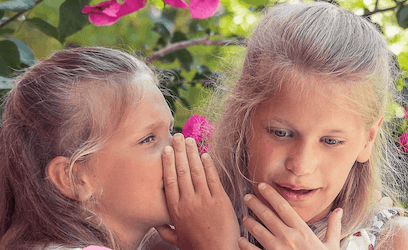 Girl whispering into the ear of another girl who can know she does not have hearing loss if she can hear well